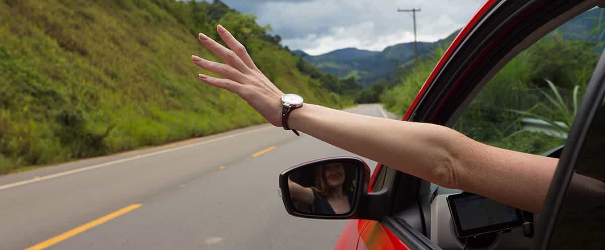 Un braccio che sporge dal finestrino di un'auto in movimento su una strada di campagna.   