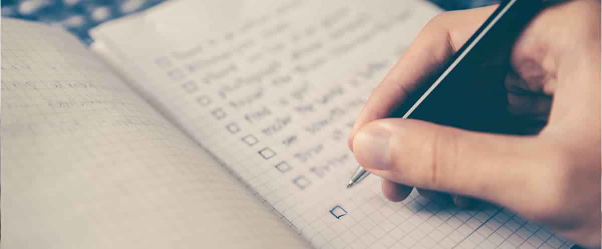 Mano che spunta con una penna una checklist su un quaderno a quadretti.