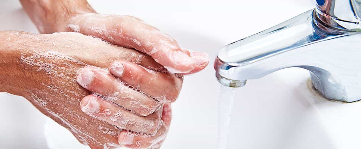 Primo piano di due mani, coperte di schiuma di sapone, che vengono lavate sotto un rubinetto d'acqua corrente