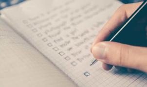 Mano che spunta con una penna una checklist su un quaderno a quadretti.