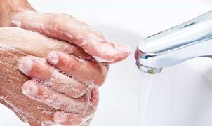 Primo piano di due mani, coperte di schiuma di sapone, che vengono lavate sotto un rubinetto d'acqua corrente